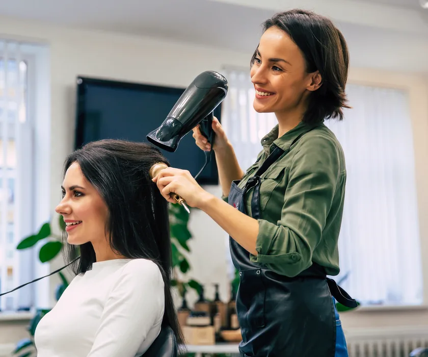 Stylistin föhnt einer lächelnden Kundin am Behandlungsplatz die Haare
